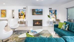 A modern living room with a fireplace, white walls, and a teal sofa. - Blue Door at Indian Canyons – Mid-Century Retreat with Pool, Spa, Golf Course and Mountain Views (Palm Springs)