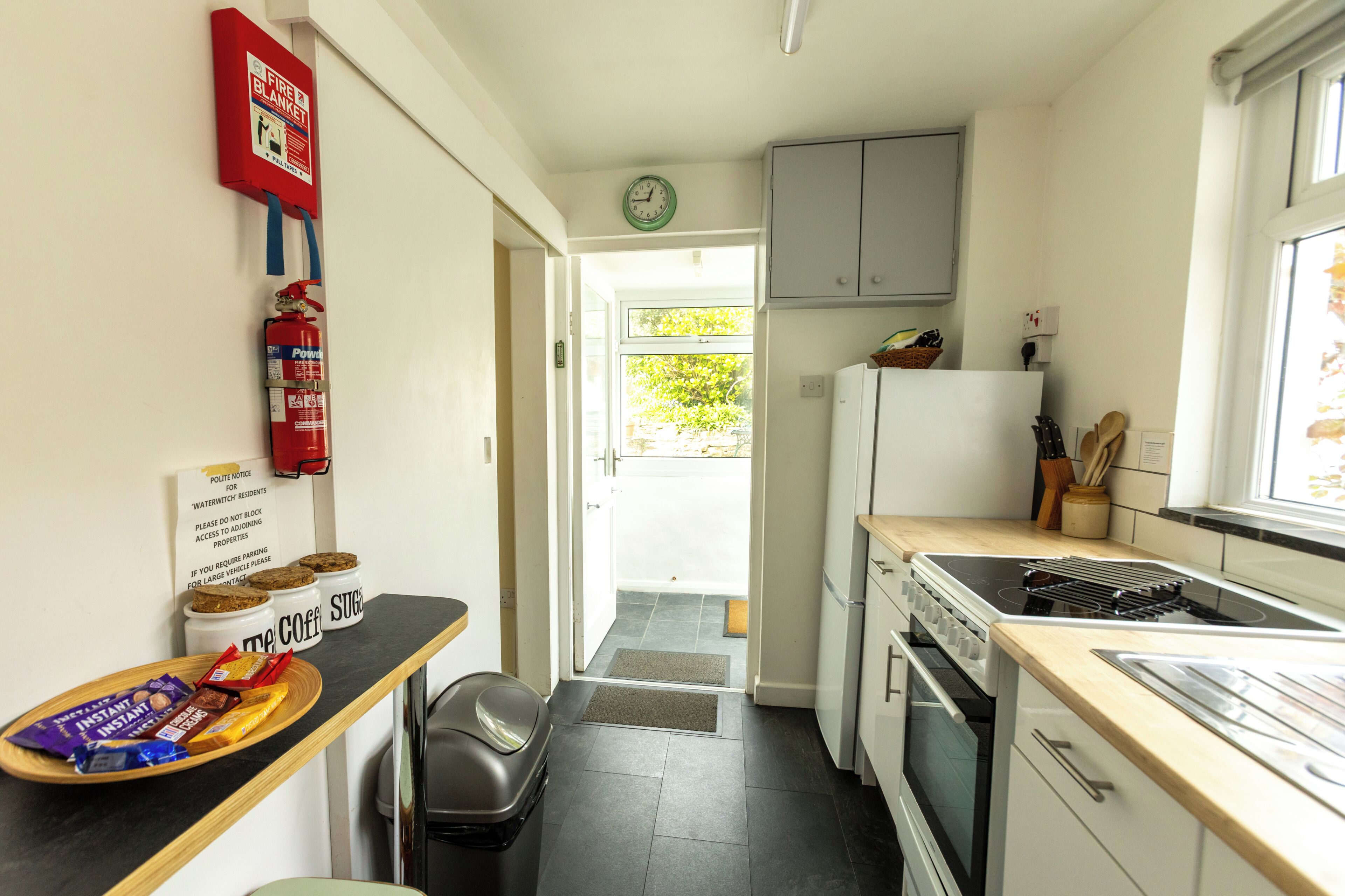 A kitchen with a fire extinguisher, a clock, cabinets, a stove, and a refrigerator.