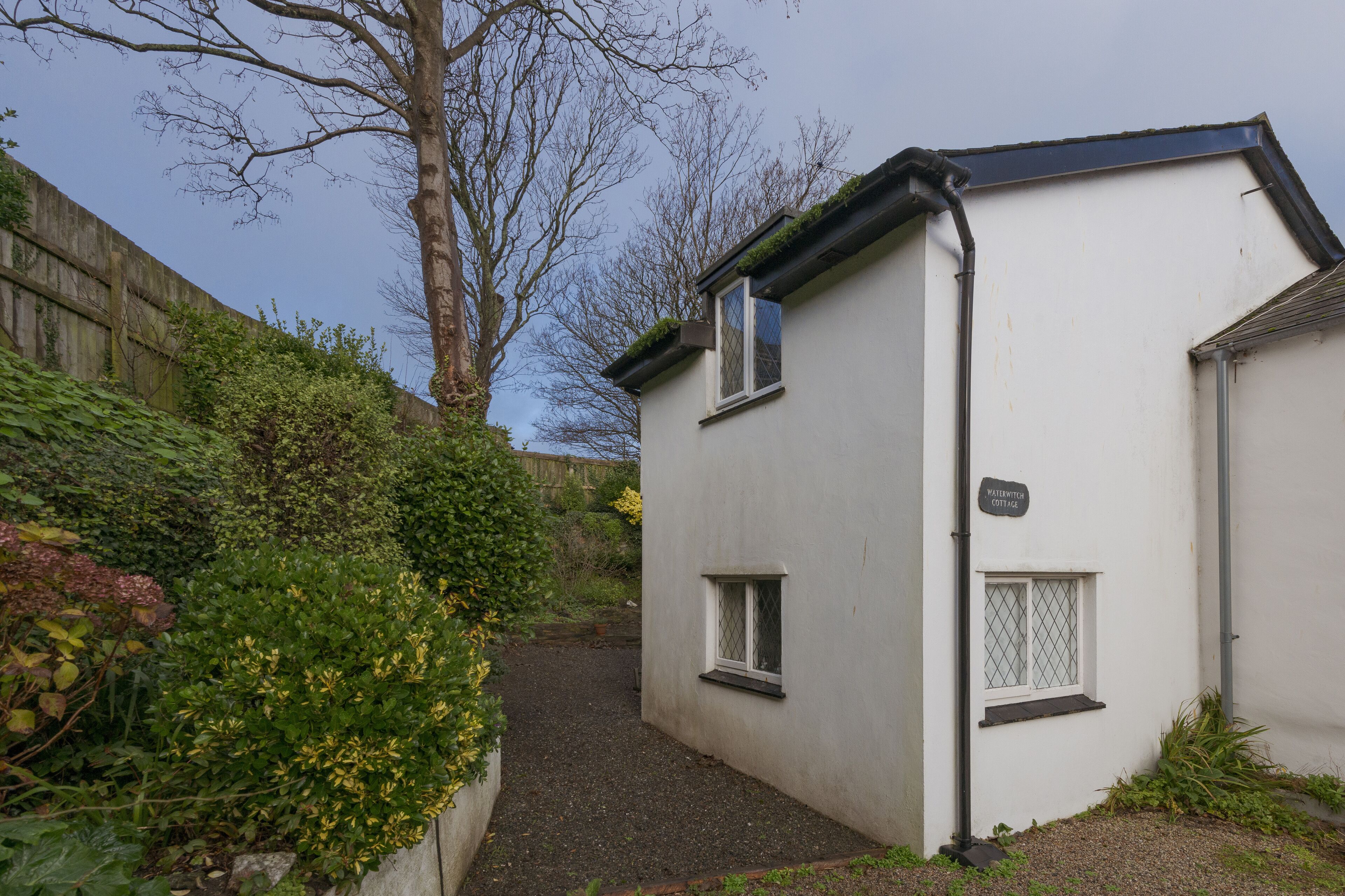 A narrow pathway leading to a white building with two windows and a small door.