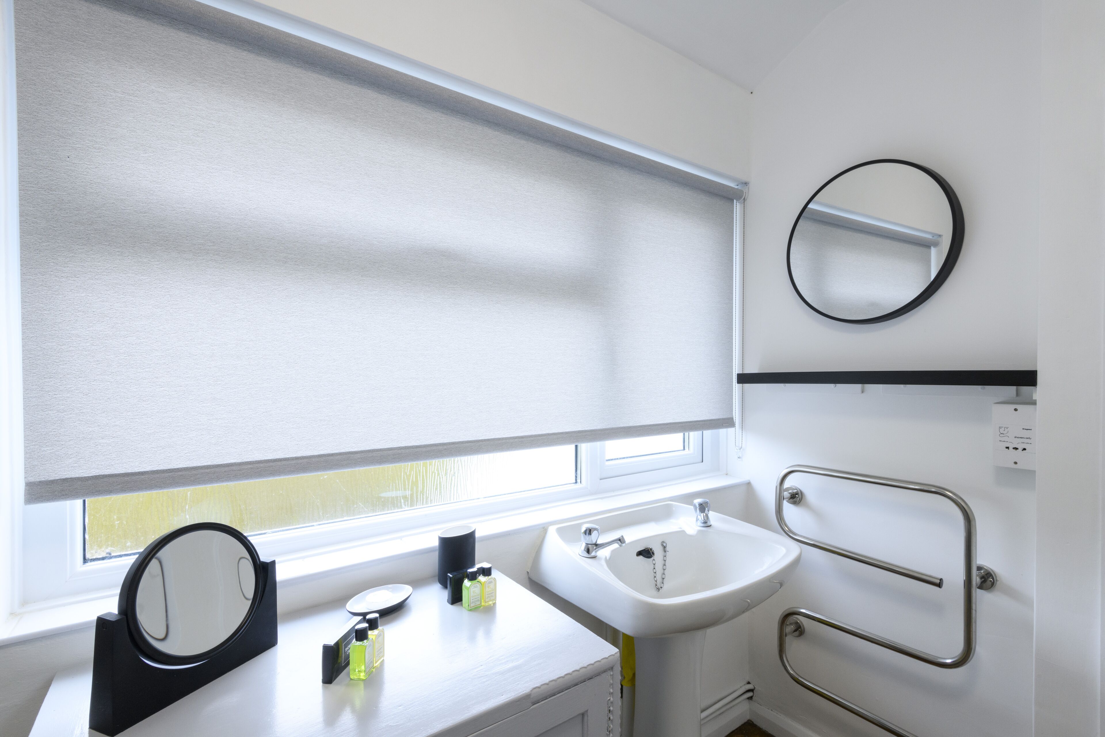 A bathroom with a window, a sink, a mirror, and a towel rack.