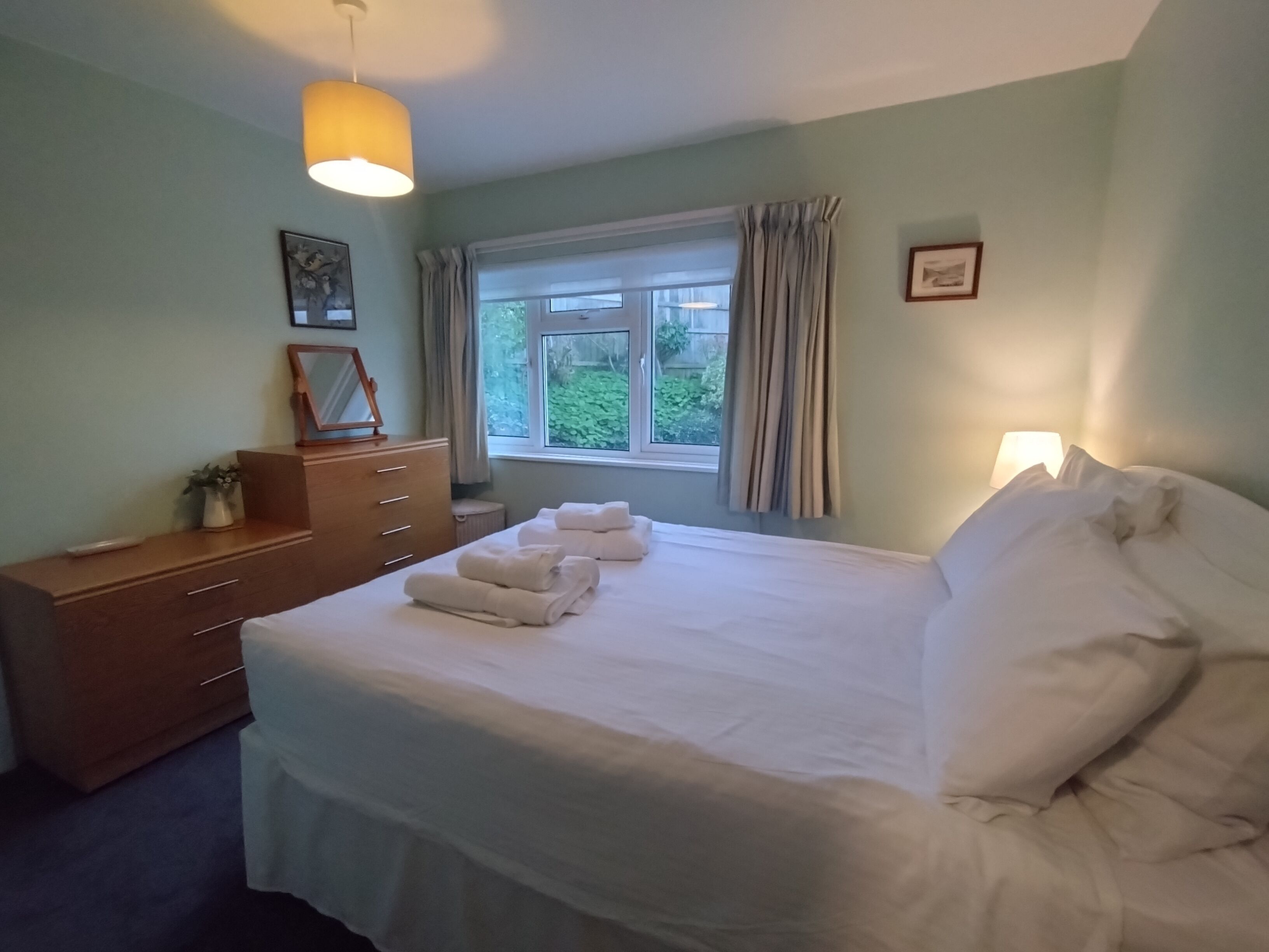 Une chambre à coucher avec un lit, une commode, une fenêtre avec des rideaux et une lampe.