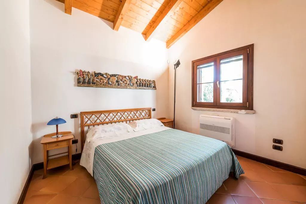 A bedroom with a bed, a nightstand, a lamp, a window, and a wall decoration.