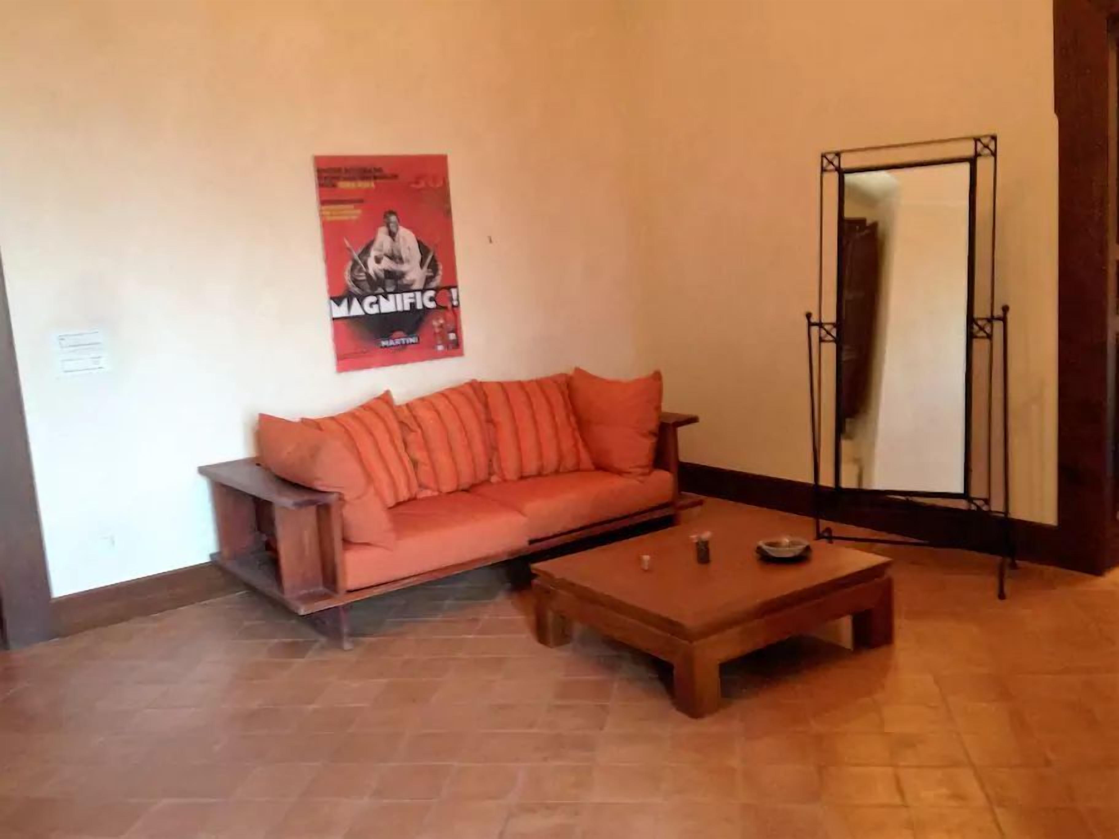 Una habitación con un sofá de madera y una pequeña mesa de madera, un cartel en la pared y un soporte de metal.