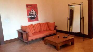 Una habitación con un sofá de madera y una pequeña mesa de madera, un cartel en la pared y un soporte de metal.