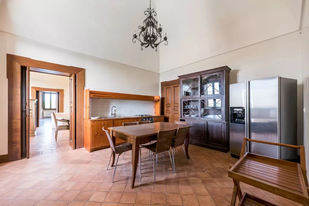 A spacious kitchen with a dining table, wooden chairs, a chandelier, and a refrigerator.