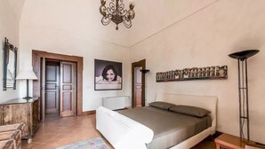 Ein Schlafzimmer mit Bett, Schreibtisch, Stuhl, Lampe, einer Kristallleuchter und einer Tür.