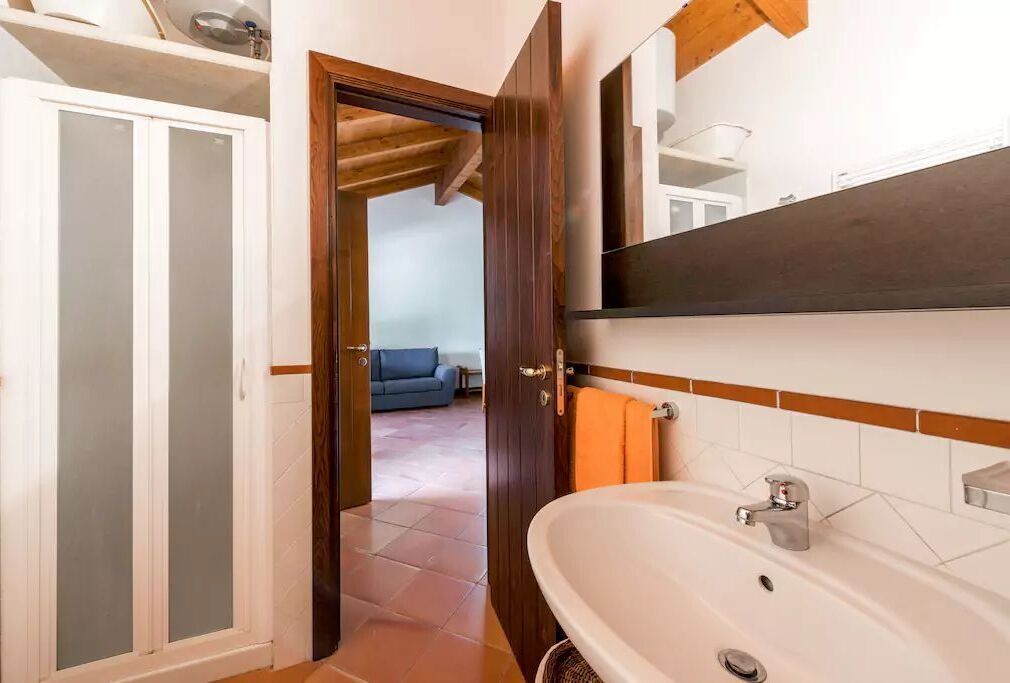 A bathroom with a white sink, a mirror, and a wooden door leading to a living room.