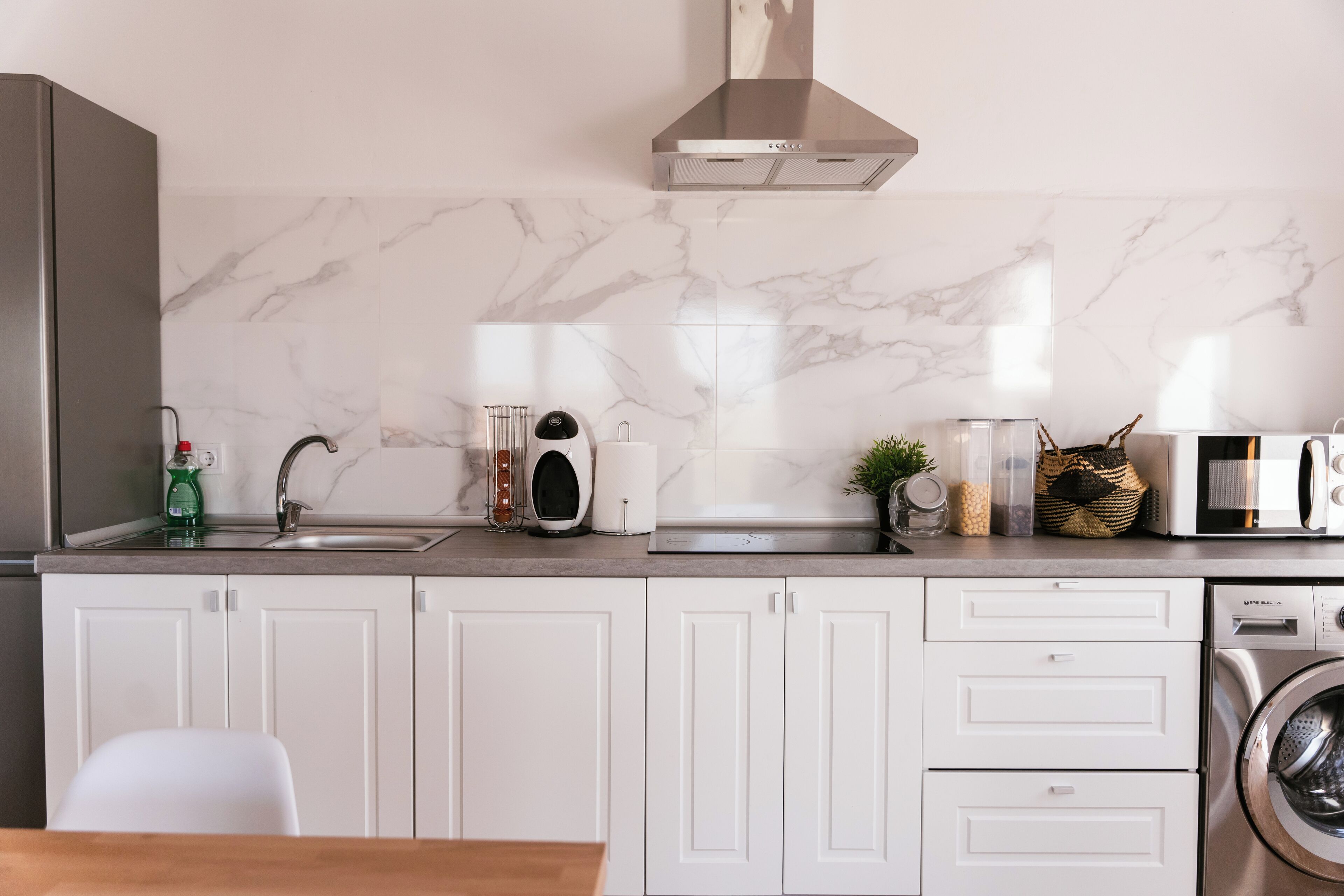 Una cocina moderna con armarios blancos, una campana extractora de acero inoxidable, un microondas y una lavadora.