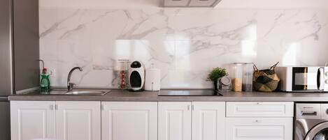 Una cocina moderna con armarios blancos, una campana extractora de acero inoxidable, un microondas y una lavadora.