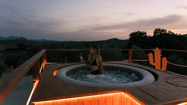 Een hottub met een houten terras en een cactusdecoratie, omgeven door een schilderachtig landschap.