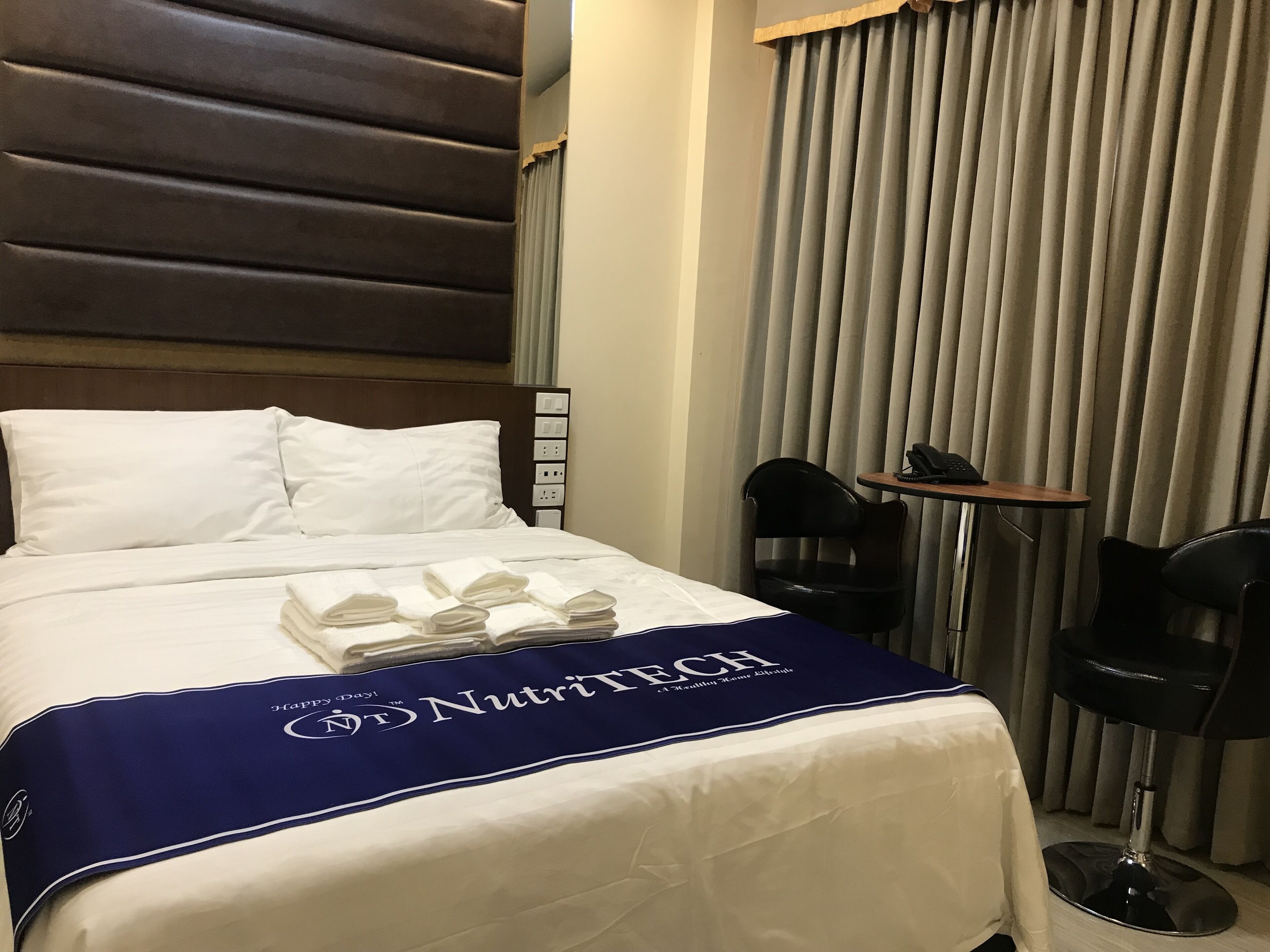A hotel room with a neatly made bed, a bedside table with a lamp, and a chair.