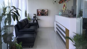 A modern living room with a black sofa, a coffee table, and a TV. There are potted plants and a decorative wall clock. - NutriTECH Hotel and Events (Calapan)