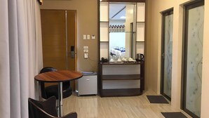 A compact hotel room with a wooden table, a small refrigerator, a minibar, and a glass door. - NutriTECH Hotel and Events (Calapan)