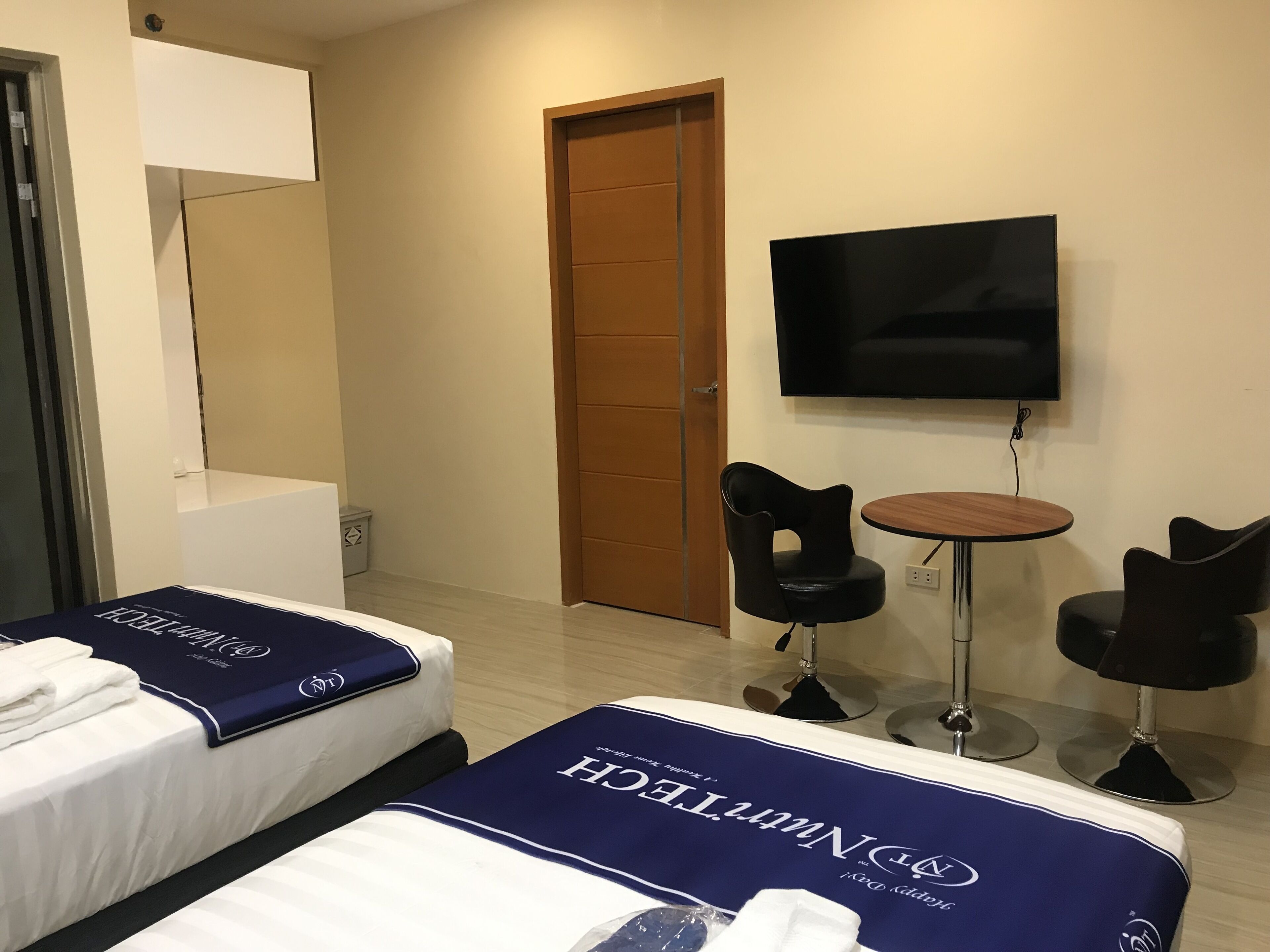 A hotel room with two beds, a TV, a small table, two chairs, and a door.