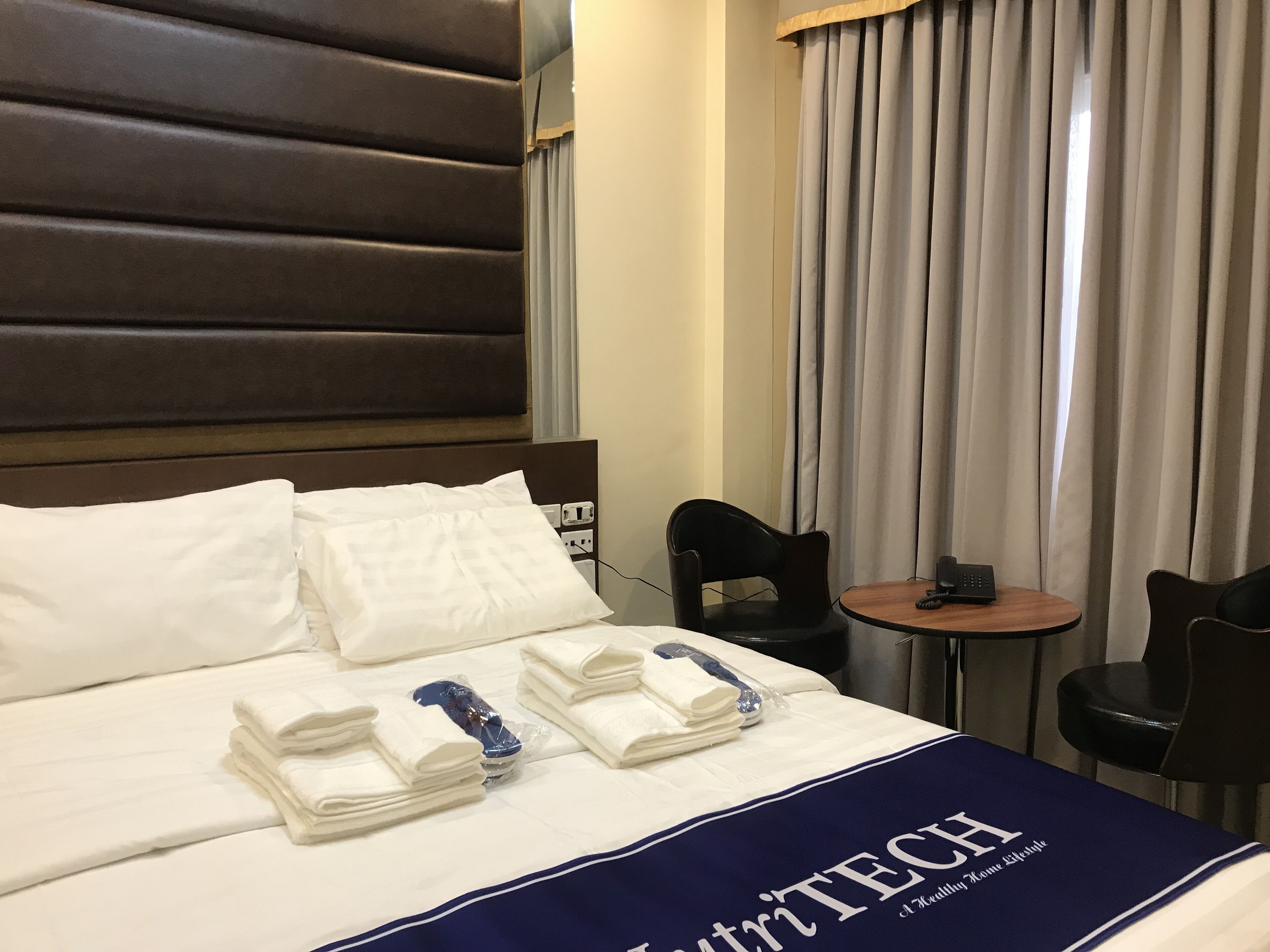 Een hotelkamer met een opgemaakt bed, een klein tafeltje met een telefoon en twee stoelen.