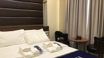 Een hotelkamer met een opgemaakt bed, een klein tafeltje met een telefoon en twee stoelen.