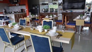 A dining area with multiple tables set for service, chairs, and a kitchen area in the background. - NutriTECH Hotel and Events (Calapan)