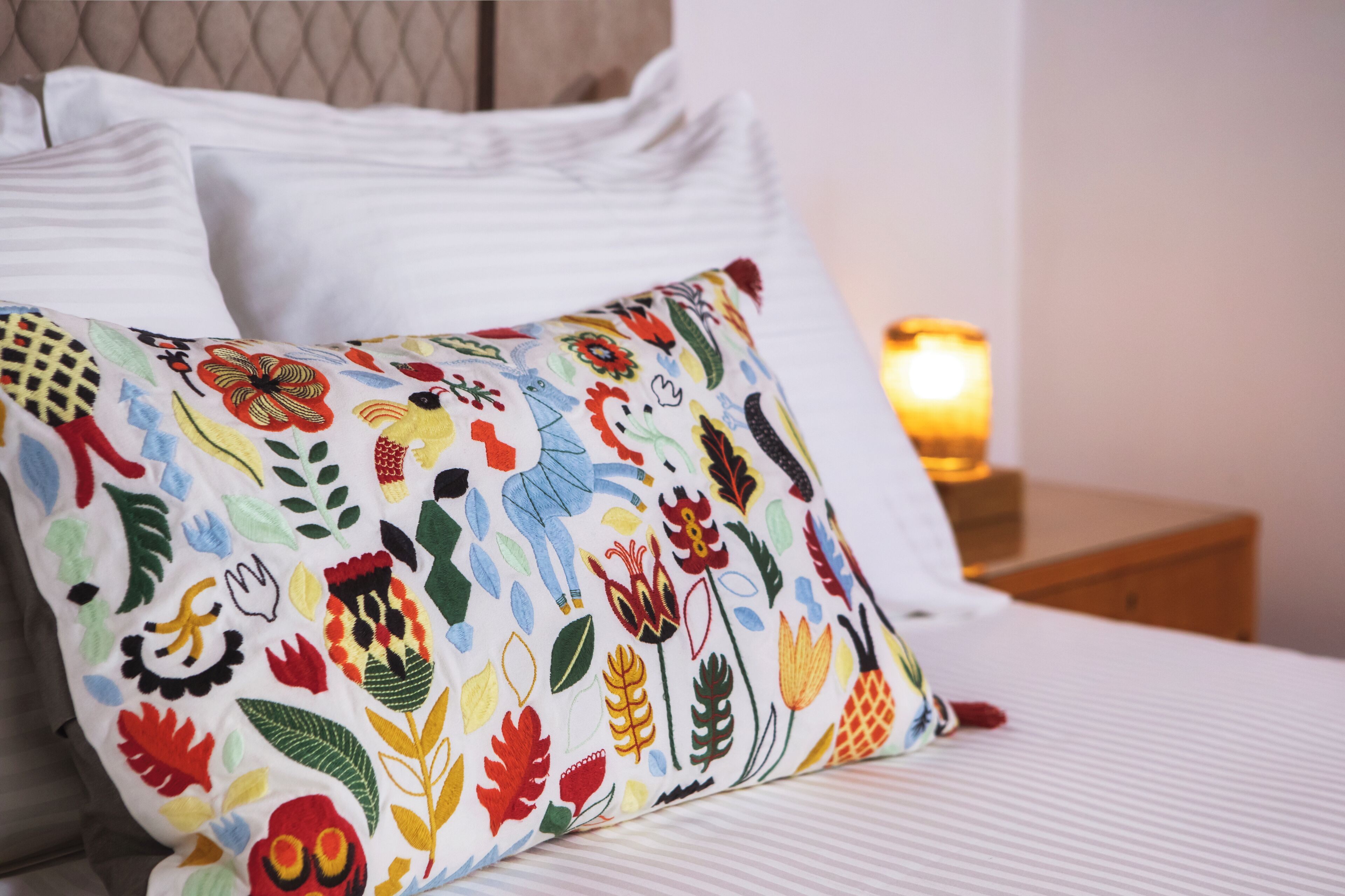 Un lit avec des oreillers blancs et un coussin coloré brodé.