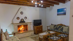 A living room with a stone fireplace, a television, a sofa, and a patterned rug. - Mikros Paradisos Pelion (Volos)