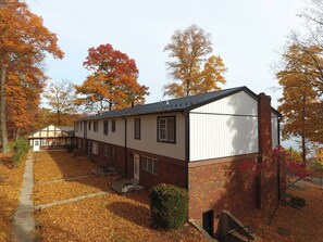 A two-story building with a brick facade and white siding, featuring a covered walkway and a small patio area.