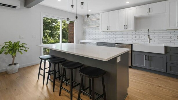 A modern kitchen with a central island, bar stools, white cabinetry, and a potted plant.
