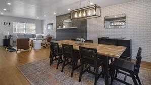A modern kitchen with a wooden table and chairs, a brick backsplash, and pendant lighting.