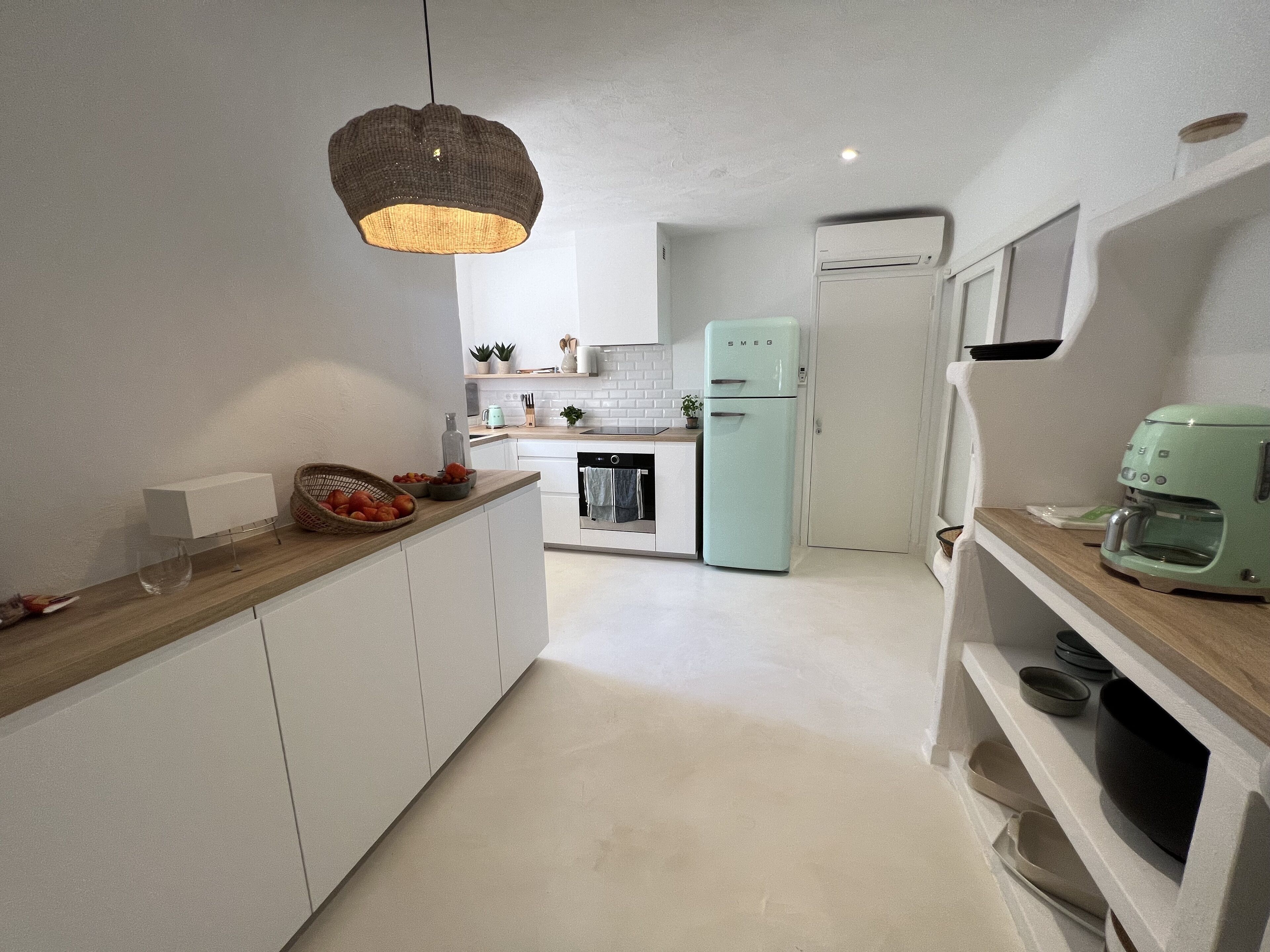 Una cocina moderna con armarios blancos, horno empotrado, refrigerador y cafetera.