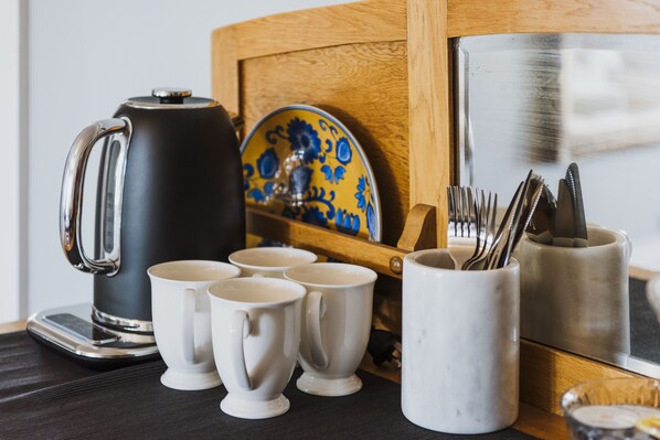 A coffee station with a black coffee maker, white cups, and a ceramic plate with blue designs.