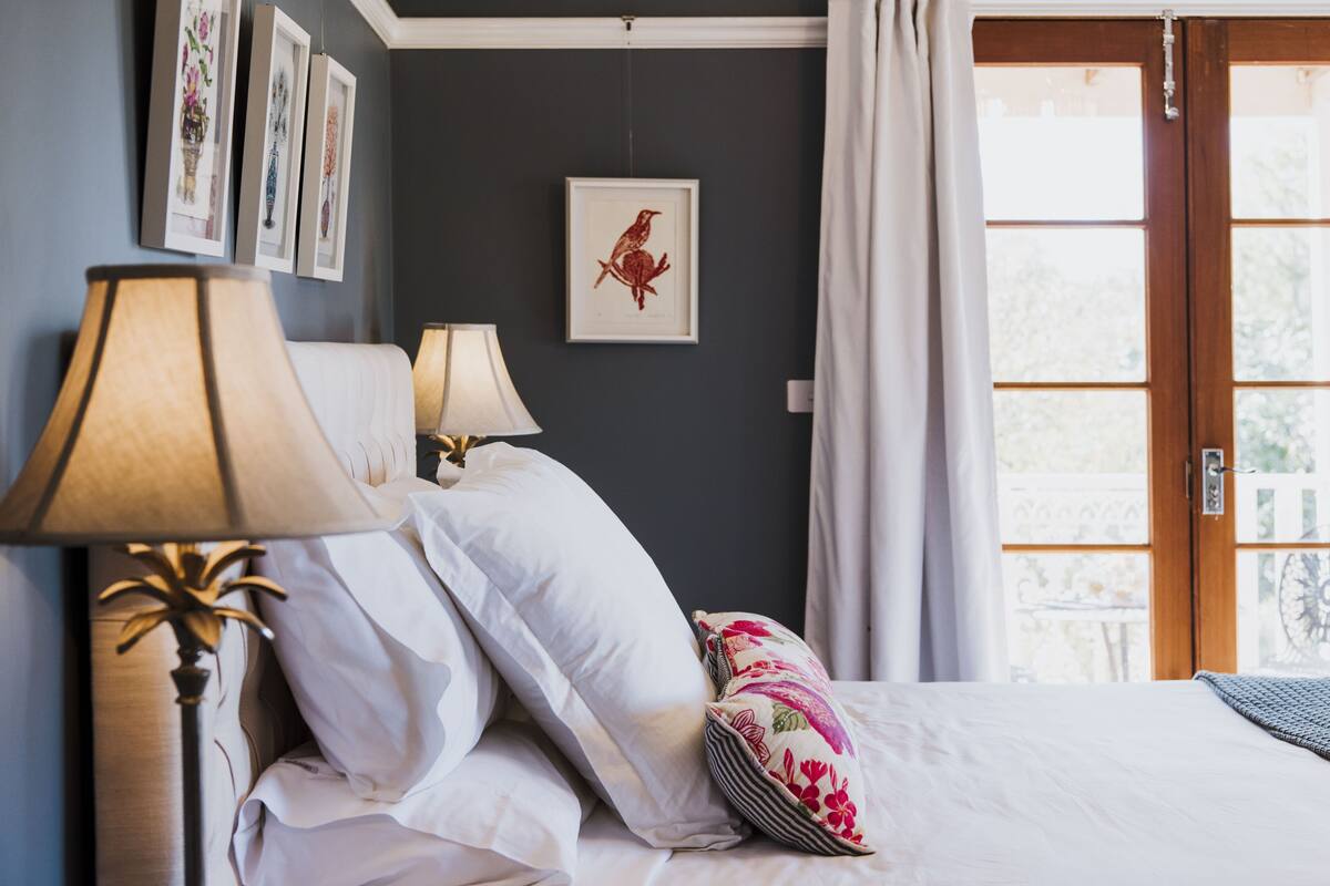 A neatly made bed with white linens and decorative pillows, a bedside lamp, and framed artwork on the wall.