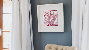 A tufted armchair with a pink throw blanket, a framed artwork on the wall, and a window with curtains.
