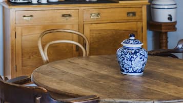 A wooden dining table with chairs, a blue and white ceramic jug, and a wooden cabinet with kitchen items.