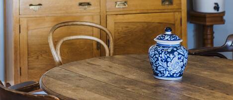 Una mesa de comedor de madera con sillas, una jarra de cerámica azul y blanca, y un mueble de madera con utensilios de cocina.