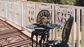 A covered outdoor seating area with a table and chairs, surrounded by a decorative fence and trees in the background.