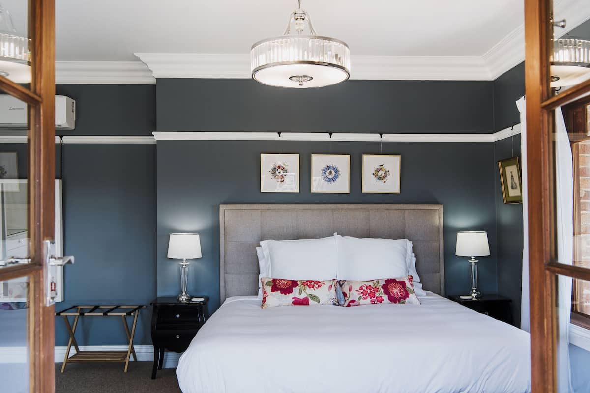A bedroom with a large bed, two bedside tables with lamps, a wooden side table, and a ceiling light fixture.