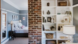 A bedroom with a brick partition, a white bookshelf, and a bed with white bedding. - Enfield House (Menah)