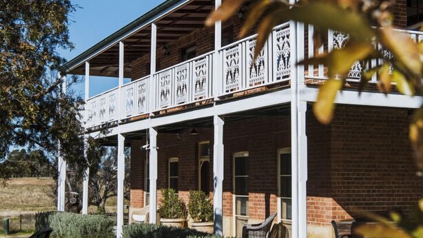 A two-story building with a covered porch and a brick facade. - Enfield House (Menah)