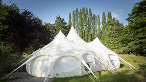 A large, white, dome-shaped tent with multiple entry points, set in a grassy area with trees in the background. - 8-bed Lotus Belle Mahal Tent in The Wye Valley (Ross-on-Wye)