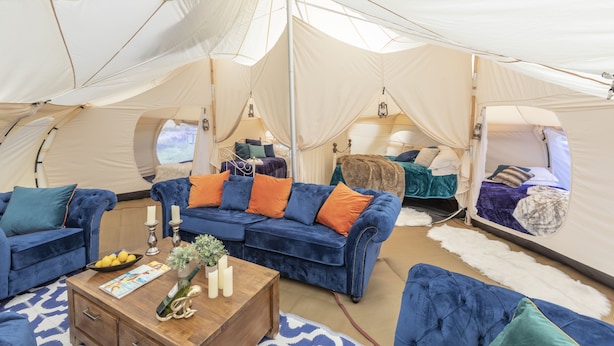A tented accommodation with a blue sofa set, a wooden coffee table, and a mirror. - 8-bed Lotus Belle Mahal Tent in The Wye Valley (Ross-on-Wye)