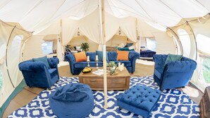 A tented accommodation with a central seating area featuring blue sofas and ottomans, a wooden coffee table, and patterned floor mats. - 8-bed Lotus Belle Mahal Tent in The Wye Valley (Ross-on-Wye)
