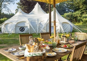 A tented outdoor dining area with a table set for a meal, surrounded by greenery. - 8-bed Lotus Belle Mahal Tent in The Wye Valley (Ross-on-Wye)