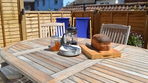 Uma mesa de madeira redonda com pão, cafeteira, pratos e talheres.