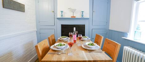 A dining room with a wooden table set for four, flanked by light blue doors, a fireplace, and a window with a view.