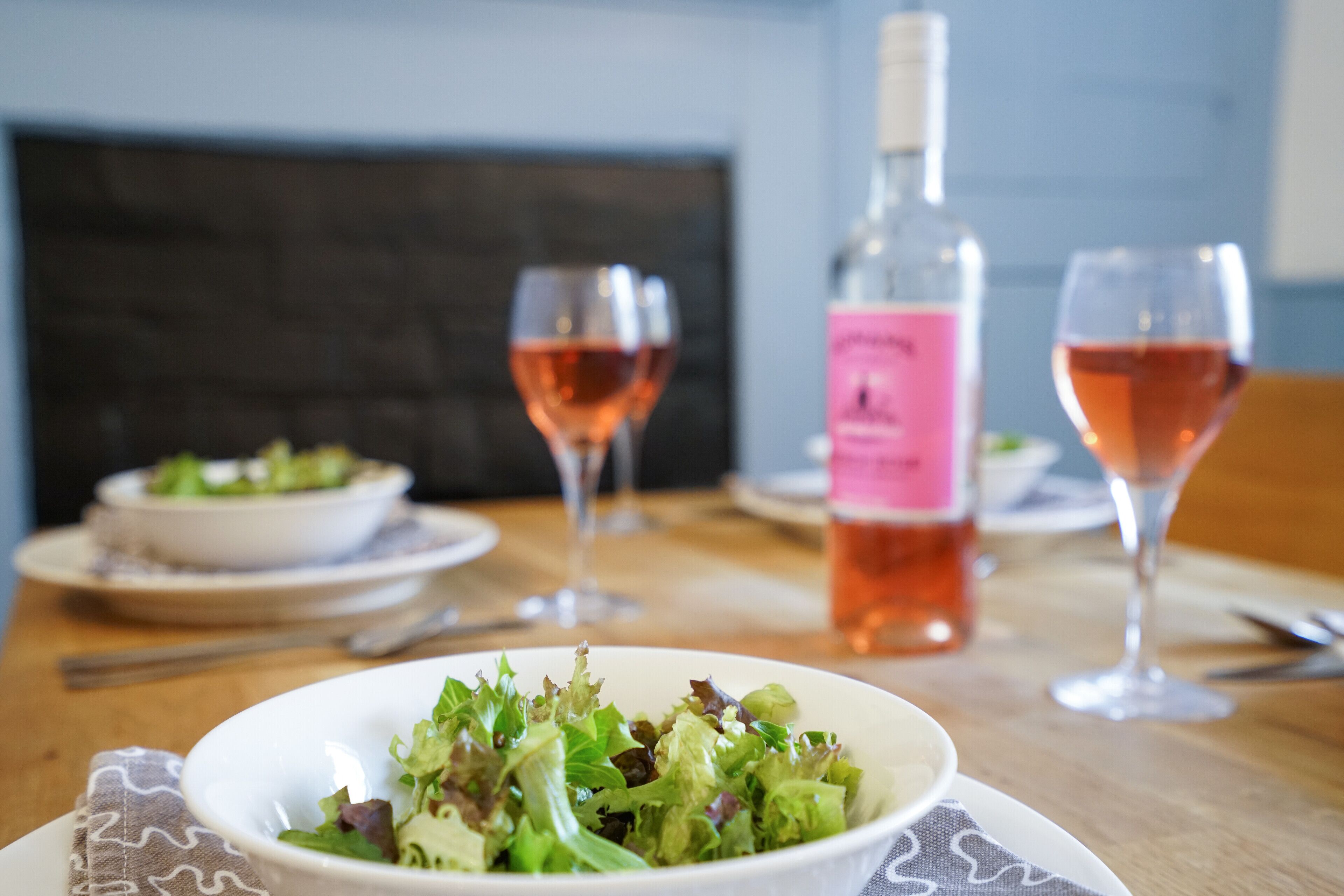 Una mesa de comedor con una ensalada en un plato, dos copas de vino y una botella.