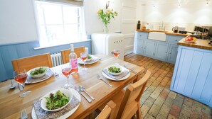 Un coin repas avec une table en bois dressée pour quatre personnes, entouré d’armoires bleues et une cuisine en arrière-plan.