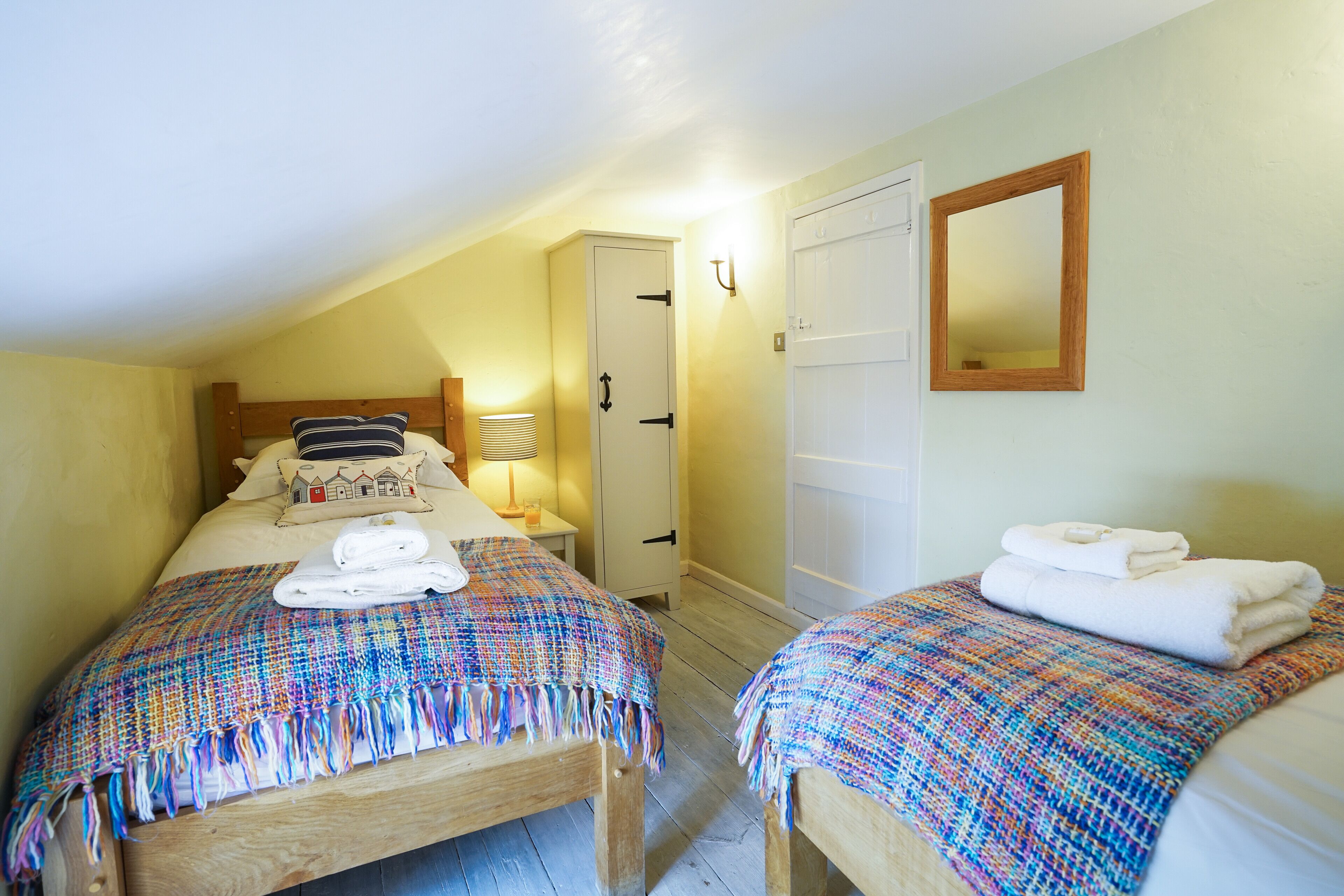 Ein Schlafzimmer mit zwei Betten, jedes mit einer bunten gewebten Decke, einer Nachttischlampe und ordentlich gefalteten Handtüchern.