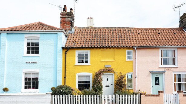 Une rangée de maisons colorées à étages, chacune présentant un style architectural distinct, avec notamment une clôture blanche en bois et un petit jardin.