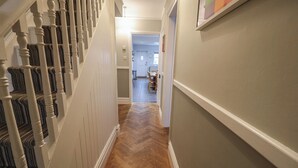 Un pasillo con suelo de madera en espiga, paredes blancas y una escalera con barandilla blanca.