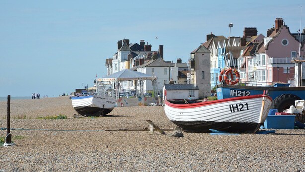A beach with several boats moored on the pebbled shore, a lifebuoy, and a building with a sign reading "South Coast". - Mariners Cottage (Aldeburgh)