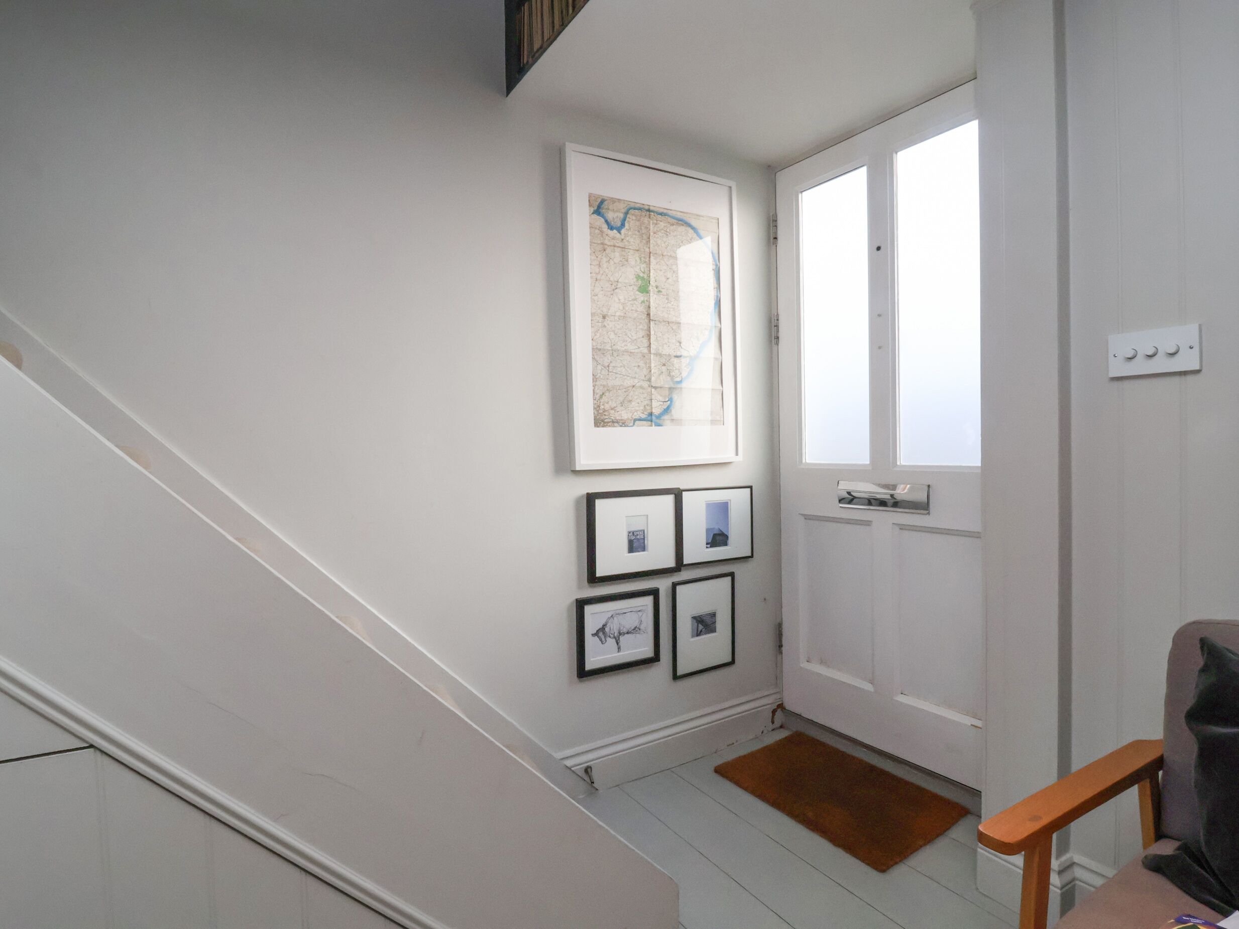 A staircase leading to a landing with a white door, a framed map, and several framed pictures on the wall.