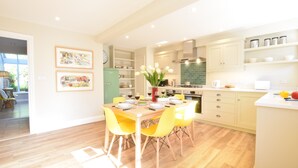 A modern kitchen with a dining area, featuring wooden flooring, yellow chairs, and a central island with a vase of flowers. - Seawall Cottage, Aldeburgh (Aldeburgh)